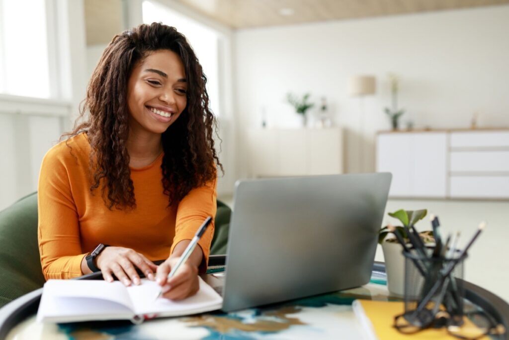 A student smiles while taking notes during an online class