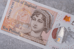 A close-up of a British ten-pound banknote featuring a detailed portrait of Jane Austen wearing a bonnet. 