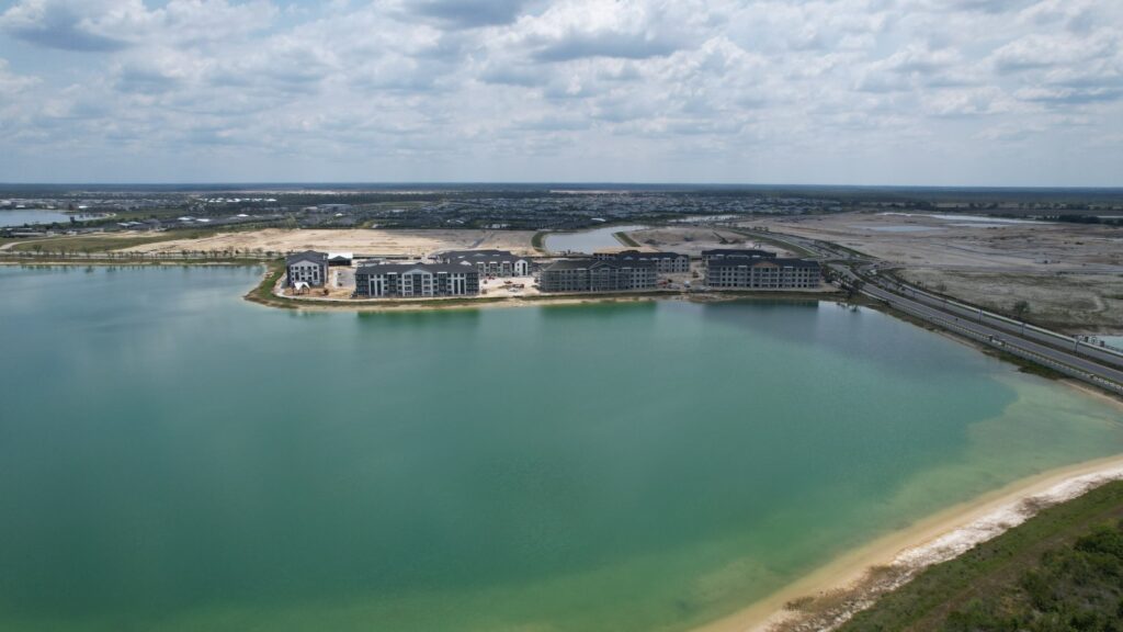 An aerial view of construction on waterfront condominiums at Babcock Ranch, with a lake in the foreground. 