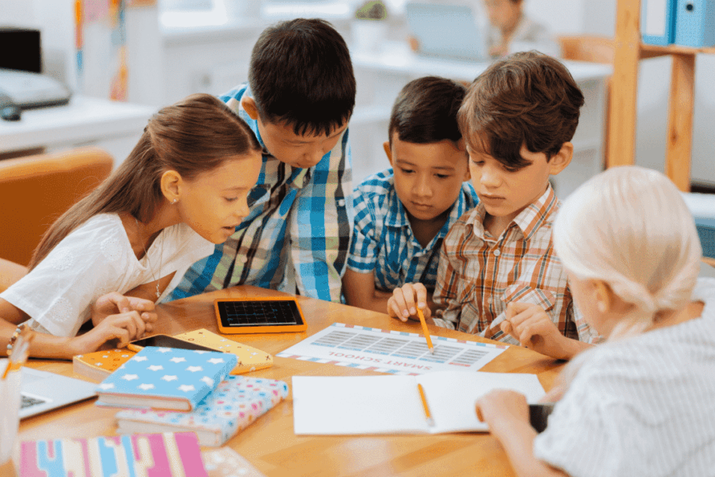 A multicultural group of elementary school students sitting around a table looking at class materials. 