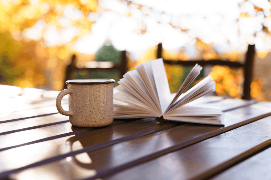 Coffee mug and open book on a sunlit table.  