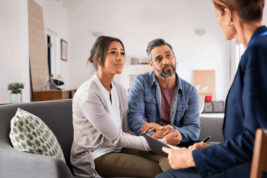 A couple holding hands while speaking with a counselor in an office setting.