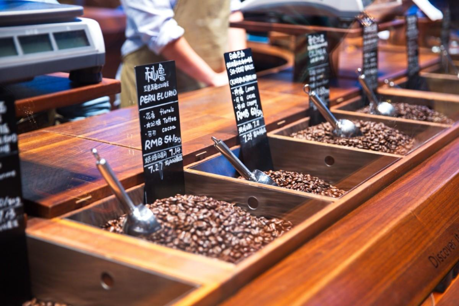Coffee shop displaying bulk international coffee beans with multilingual labels and local pricing. 