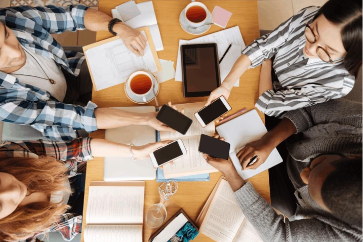 Overhead view of young adults sitting around a table using smartphones. 
