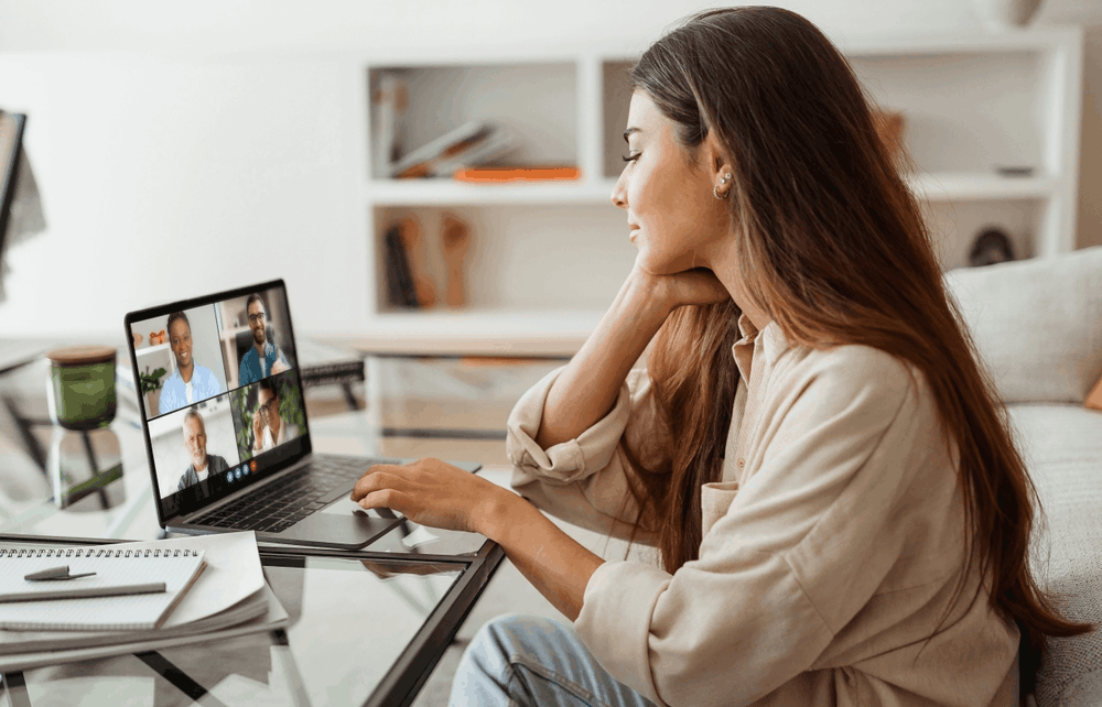 A woman sits on the floor while taking a video call with four colleagues on her laptop at home.