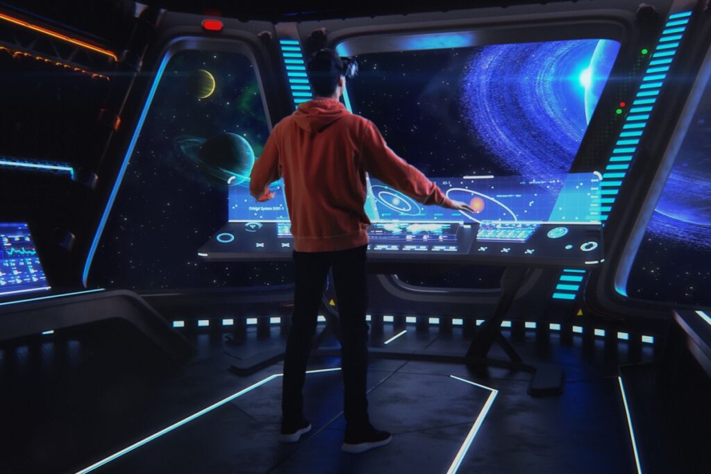 Person in a VR headset stands at a holographic control panel in an immersive spaceship environment.