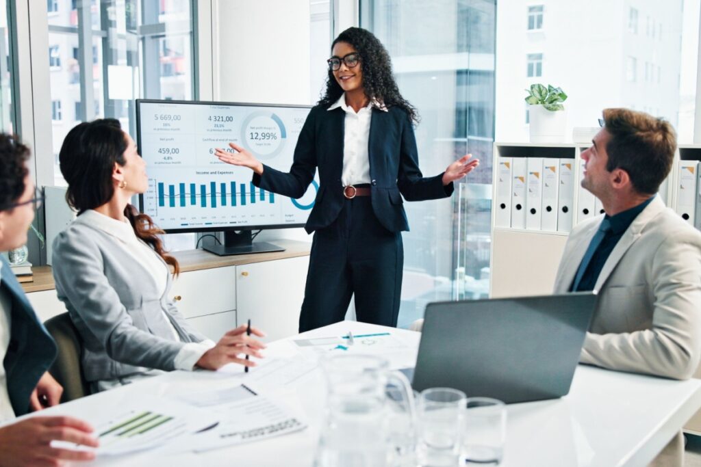 A woman in a navy suit presents data charts to four colleagues in a conference room.