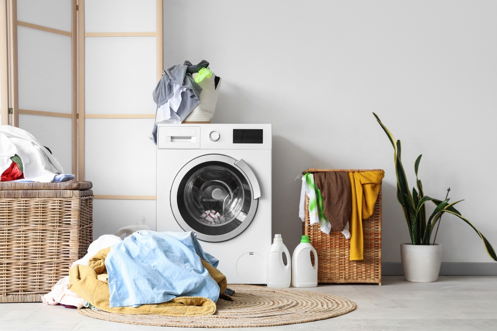 Unfolded laundry piled around a washing machine and laundry baskets